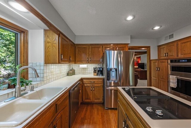 12224 Connell Dr, Overland Park, KS 66213 - kitchen with appliances with stainless steel finishes, a textured ceiling, dark wood finished floors, brown cabinetry, and recessed lighting