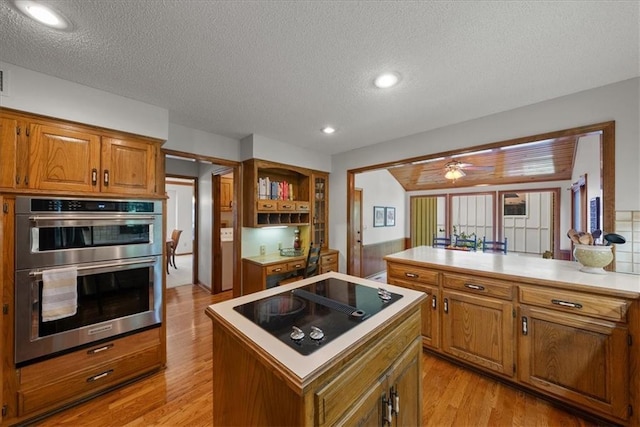 12224 Connell Dr, Overland Park, KS 66213 - kitchen featuring double oven, black electric stovetop, brown cabinets, light wood-style floors, and a center island