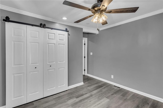 6531 W 49th St, Mission, KS 66202 - unfurnished bedroom with a barn door, baseboards, a closet, ornamental molding, and wood finished floors