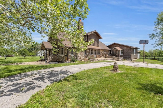 view of front of property featuring curved driveway, stone siding, a front yard, and a chimney