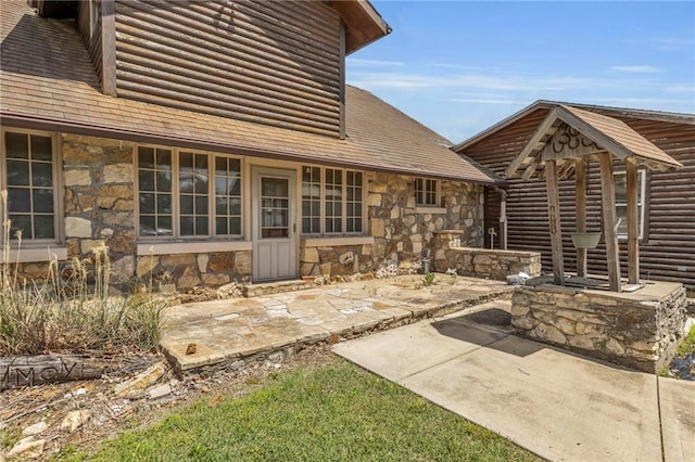 rear view of house with stone siding, a patio, log veneer siding, and roof with shingles