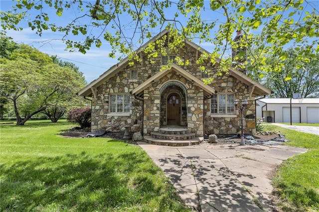 view of front of house with stone siding, a front lawn, an outbuilding, and a detached garage