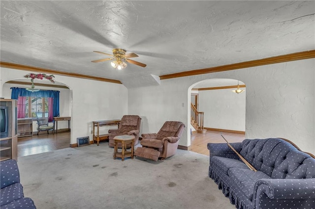 living area featuring arched walkways, crown molding, stairs, ceiling fan, and a textured ceiling