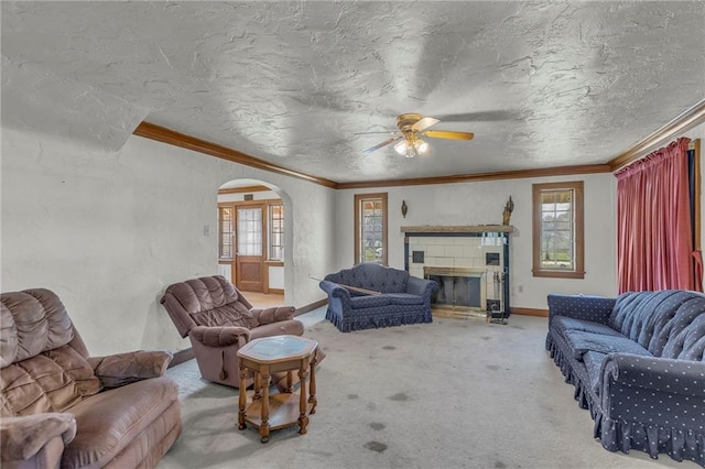 carpeted living area with ornamental molding, arched walkways, ceiling fan, a glass covered fireplace, and a textured ceiling