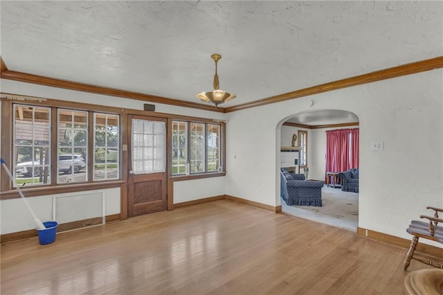 unfurnished living room featuring arched walkways, wood finished floors, baseboards, ornamental molding, and a textured ceiling