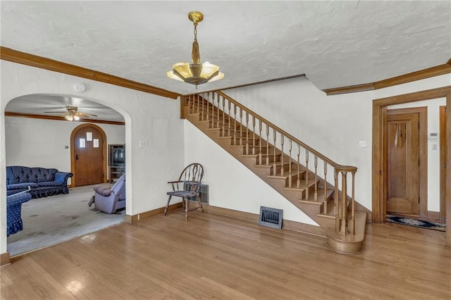 unfurnished living room featuring arched walkways, wood finished floors, stairs, crown molding, and ceiling fan