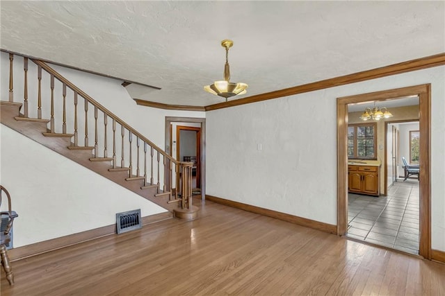unfurnished living room with hardwood / wood-style flooring, a chandelier, stairs, ornamental molding, and baseboards