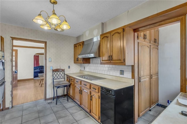 kitchen featuring black electric stovetop, light countertops, wall chimney exhaust hood, a chandelier, and arched walkways