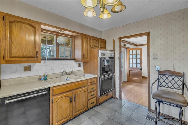 kitchen featuring dishwashing machine, double oven, a sink, light countertops, and a chandelier