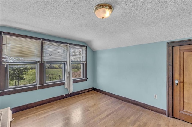 empty room featuring a textured ceiling, light wood-style flooring, baseboards, and vaulted ceiling