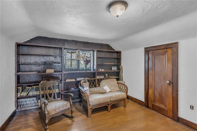 sitting room with lofted ceiling, baseboards, wood finished floors, a textured ceiling, and built in shelves