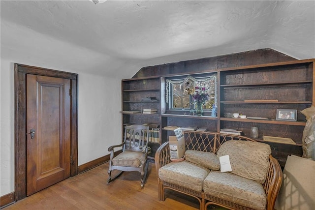 living area featuring baseboards, wood finished floors, vaulted ceiling, and built in shelves