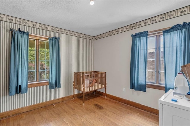 bedroom featuring wood finished floors, baseboards, washer / dryer, and a textured ceiling