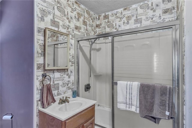 bathroom with wallpapered walls, a textured ceiling, vanity, and combined bath / shower with glass door