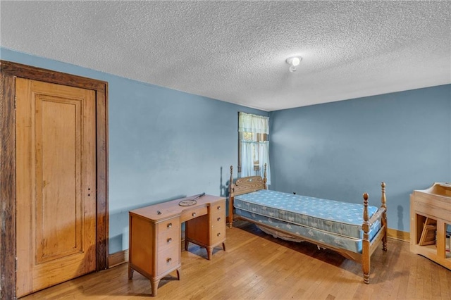 bedroom featuring wood finished floors, a textured ceiling, and baseboards