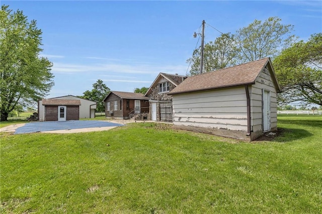 rear view of house with an outbuilding, a yard, and roof with shingles