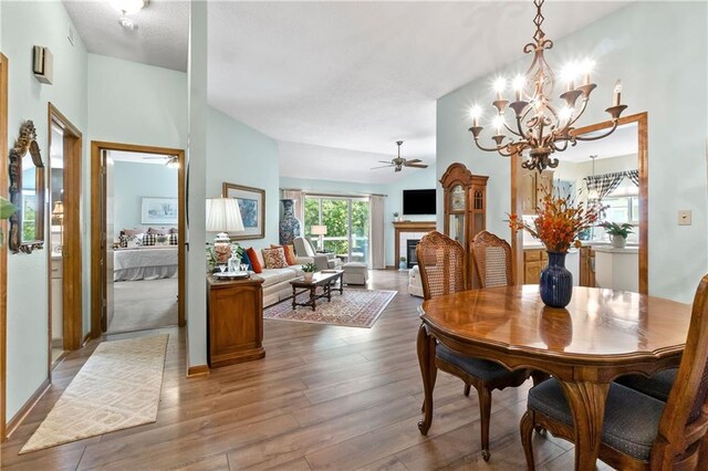 dining room featuring wood finished floors, ceiling fan, a chandelier, and a tile fireplace