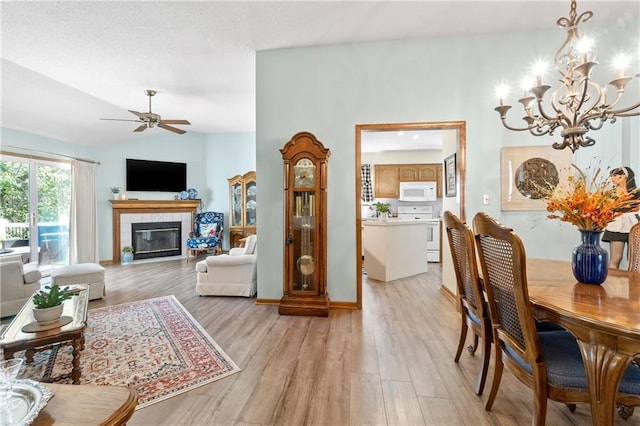living room with a chandelier, a ceiling fan, light wood-style floors, a tiled fireplace, and lofted ceiling