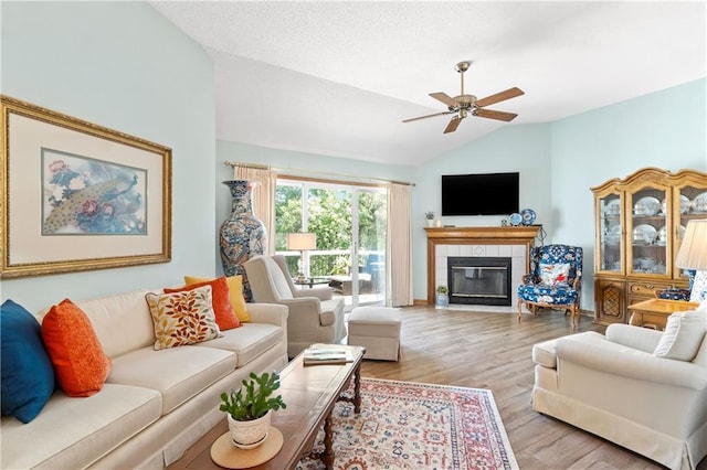 living area featuring vaulted ceiling, a ceiling fan, light wood-style floors, a tiled fireplace, and baseboards