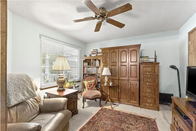 living area with light colored carpet, ceiling fan, and a textured ceiling
