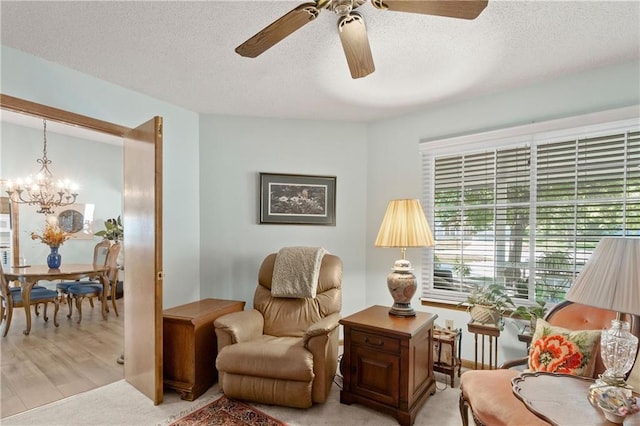 sitting room with a ceiling fan, a chandelier, a textured ceiling, and light colored carpet