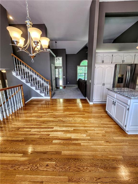 unfurnished living room featuring a chandelier, light wood-type flooring, baseboards, and stairway