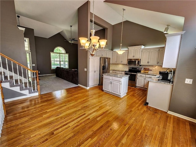kitchen with appliances with stainless steel finishes, a kitchen island, light wood-style flooring, open floor plan, and backsplash