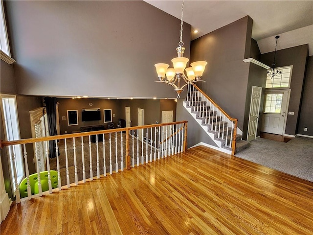 unfurnished living room with a high ceiling, a chandelier, baseboards, and wood finished floors