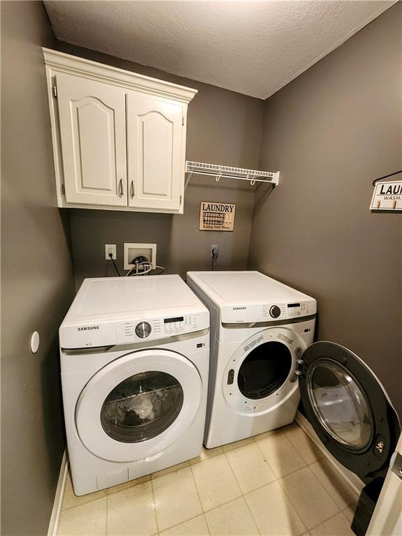 washroom featuring cabinet space, separate washer and dryer, a textured ceiling, light tile patterned flooring, and baseboards
