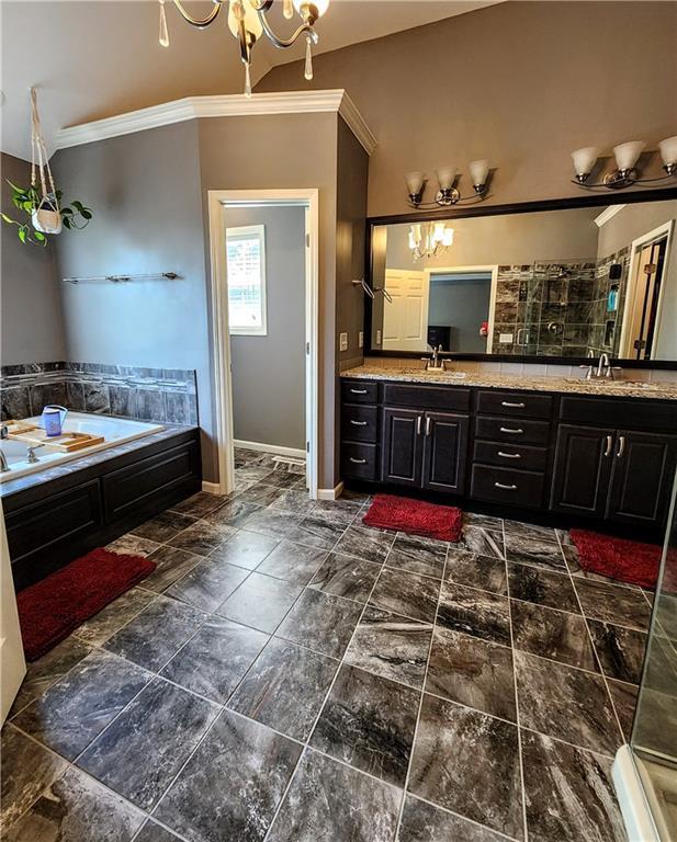 full bath with ornamental molding, a chandelier, double vanity, a garden tub, and baseboards