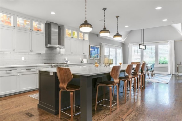 2807 W 50th Ter, Westwood, KS 66205 - kitchen featuring wall chimney range hood, light countertops, decorative backsplash, an island with sink, and white cabinetry
