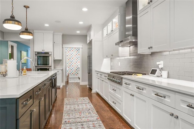 2807 W 50th Ter, Westwood, KS 66205 - kitchen featuring wall chimney range hood, appliances with stainless steel finishes, white cabinetry, a sink, and dark wood finished floors