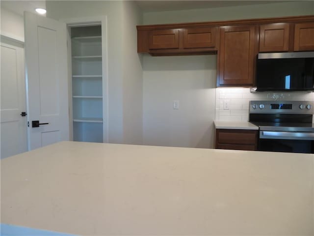 902 2nd St, Perry, KS 66073 - kitchen with stainless steel electric stove, tasteful backsplash, light countertops, and brown cabinetry