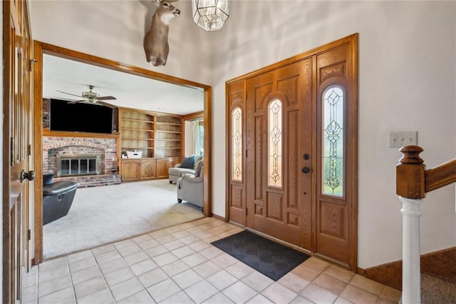 foyer with light carpet, a brick fireplace, baseboards, a ceiling fan, and light tile patterned floors
