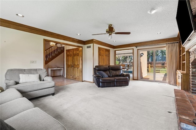 carpeted living area with stairs, a fireplace, a ceiling fan, ornamental molding, and a textured ceiling