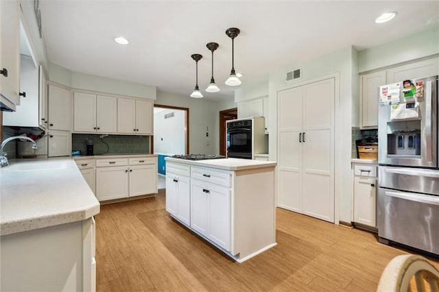 kitchen featuring stainless steel appliances, a sink, decorative backsplash, light countertops, and light wood finished floors