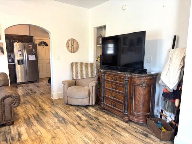 living area with arched walkways, wood finished floors, and baseboards