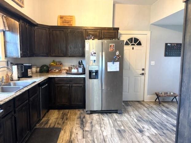 kitchen with stainless steel fridge, a sink, light countertops, light wood-style flooring, and dark brown cabinets