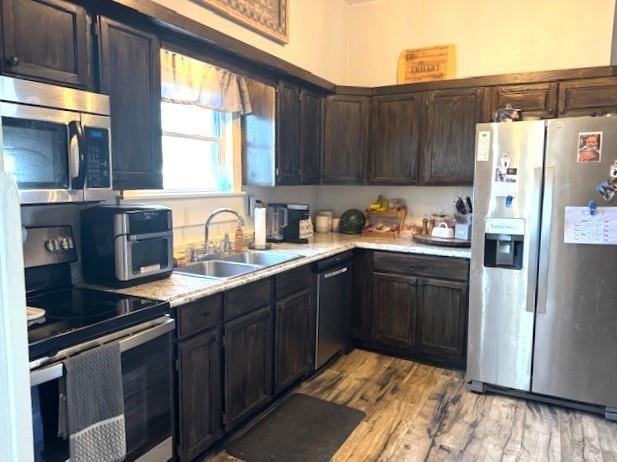 kitchen featuring appliances with stainless steel finishes, a sink, light countertops, light wood-style flooring, and dark brown cabinetry