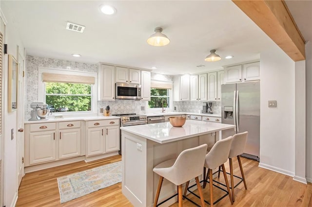 7408 Ash St, Prairie Village, KS 66208 - kitchen with stainless steel appliances, light wood finished floors, a kitchen breakfast bar, tasteful backsplash, and light countertops