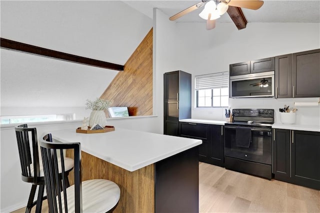 kitchen featuring black range with electric stovetop, stainless steel microwave, a breakfast bar area, light countertops, and a ceiling fan