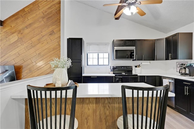 kitchen with appliances with stainless steel finishes, vaulted ceiling, ceiling fan, light countertops, and wood walls