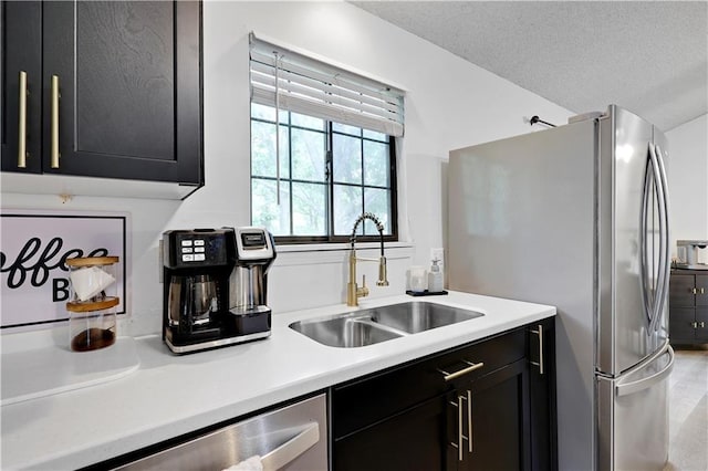 kitchen with a sink, dark cabinetry, light countertops, stainless steel appliances, and a textured ceiling