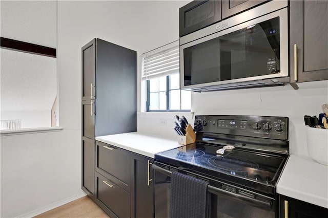 kitchen with stainless steel microwave, black electric range, light countertops, and light wood-type flooring