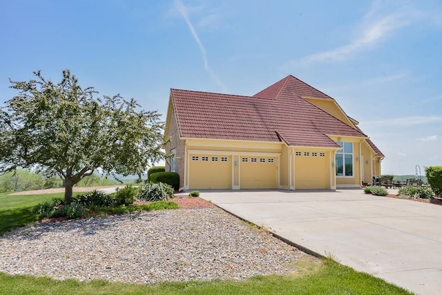 view of front facade featuring an attached garage, a tiled roof, driveway, and stucco siding