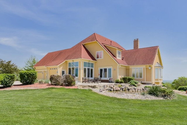 back of property featuring a chimney, stucco siding, a tiled roof, a lawn, and a patio