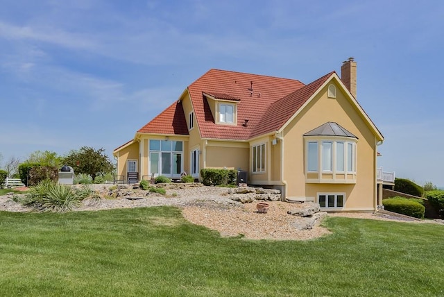 back of house featuring stucco siding, a yard, a chimney, and a tiled roof