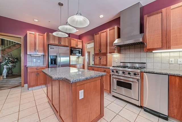 kitchen with built in appliances, wall chimney range hood, light tile patterned flooring, a kitchen island, and tasteful backsplash