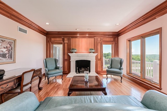 living room featuring crown molding, light wood finished floors, a fireplace with raised hearth, baseboards, and recessed lighting