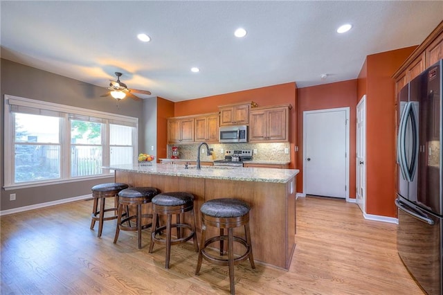 1906 Blackbird Cir, Kearney, MO 64060 - kitchen featuring appliances with stainless steel finishes, a breakfast bar area, a kitchen island with sink, light stone countertops, and decorative backsplash